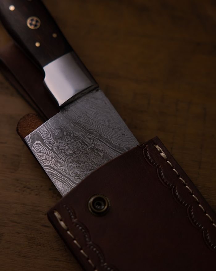 Services Detailed image of a Damascus steel knife partially encased in a crafted leather sheath.