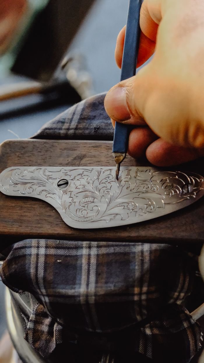 Detailed hand-engraving of metal blade by skilled artisan, showcasing craftsmanship.