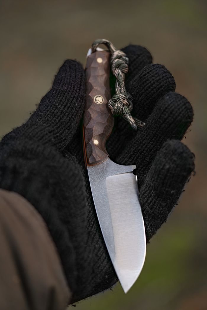 Close-up of a handmade knife held by a gloved hand, showcasing unique craftsmanship and outdoor utility.