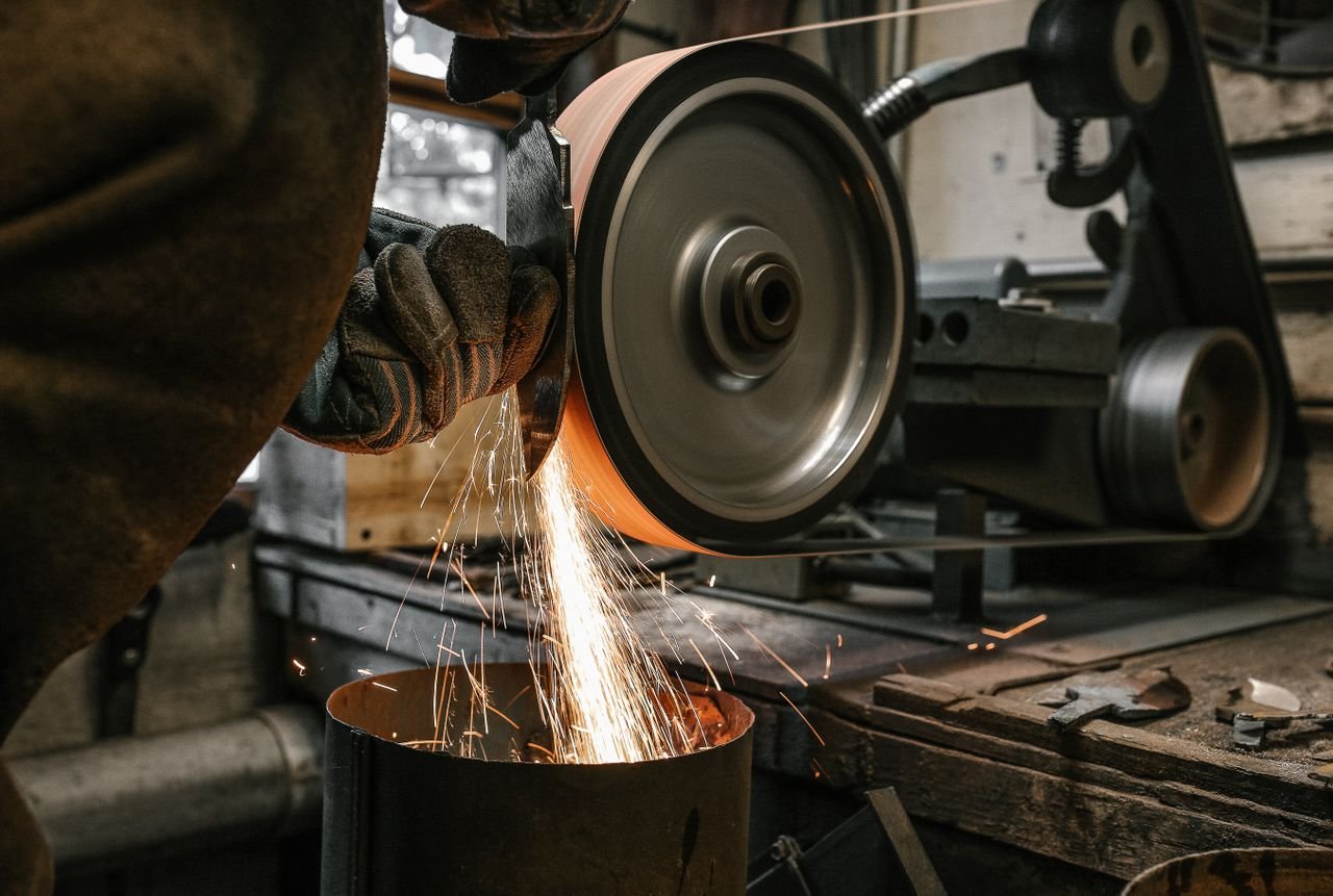 Services A close-up of a metalworker grinding a blade, creating sparks in a workshop setting.
